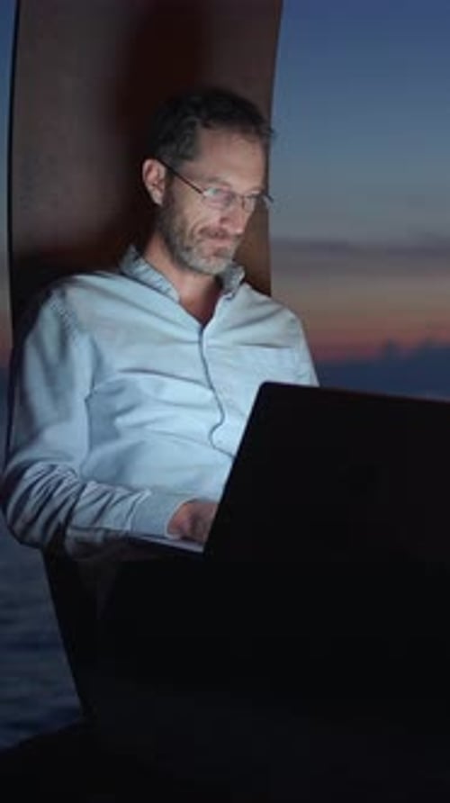 Man with Glasses Works on Laptop at Night