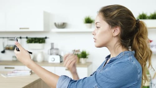 Woman applying lipstick in bright, modern kitchen