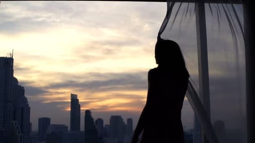 Silhouette of Woman Opening Curtains to City Sunrise