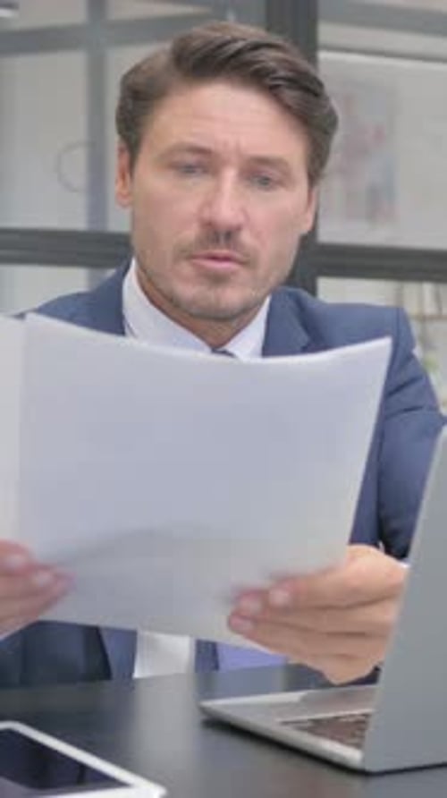 Focused Man Reviews Documents at His Office Desk