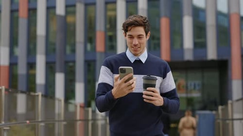 Handsome Young Business Guy Walking Outside Using His Device Holding Coffee