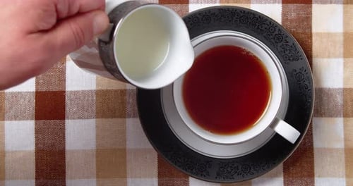 Adding Milk From a Jug to a Cup with Black Fragrant Tea Top Down View