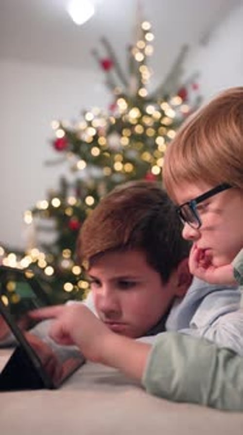 In Xmas Decorate Room Two Boy Lies on Sofa and Using Tablet