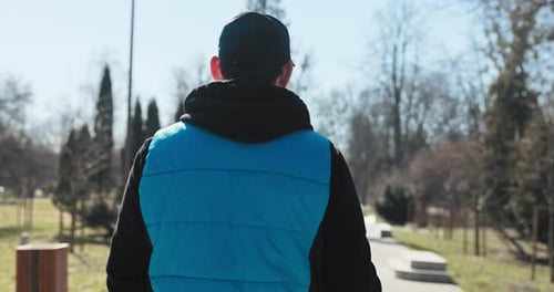 Man Walking in Park Puts on Headphones and Checks Watch
