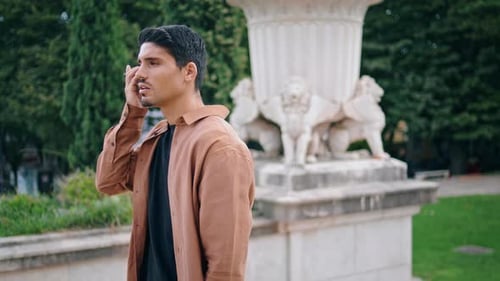 Serious Man Listening Cellphone Message in Statue Background. Hispanic Focused Guy Holding