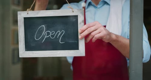 Portrait of a barman while putting the signal of open at the entrance of his bar, he smiles proud