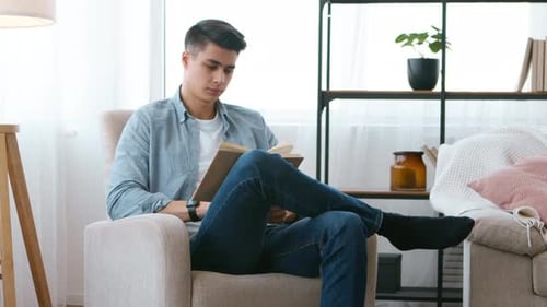 Junger Mann liest zu Hause ein Buch und wird zur nächsten Seite