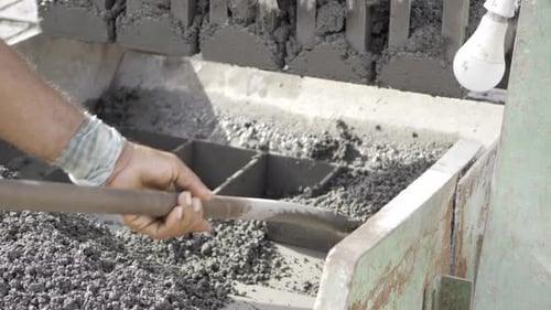 Worker Using Shovel to Fill Concrete Block Machine