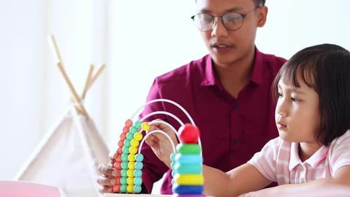 Un joven tutor en camisa enseña a una niña a contar usando cuentas, ábaco y apilando anillos