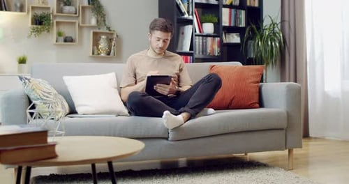 Young Man Relaxing with Tablet on Sofa at Home