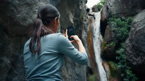 Woman Taking Photo of Waterfall in Nature