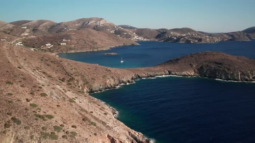 Plan de camionnage par drone de la côte grecque de Syros, eau d'un bleu profond contrastant avec un paysage montagneux sec