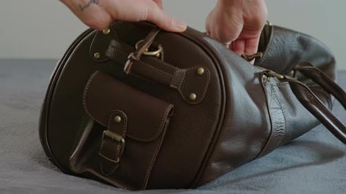Opening Brown Leather Duffel Bag on Bed
