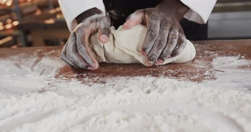Panadero afroamericano trabajando en la cocina de una panadería, amasando masa en la encimera en cámara lenta
