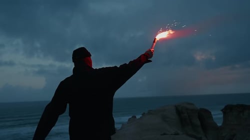 Man with red torch walking by the rocky seaside at dusk with beautiful dark blue sky