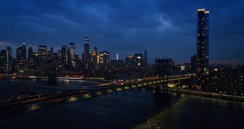 Impressive sight of night New York from the side of the river. Numerous cars ride by the bridges.