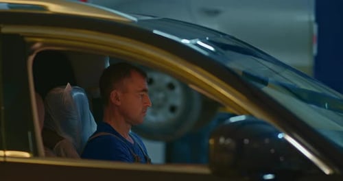Auto Mechanic Sits in the Cab of the Car and Diagnoses Malfunctions Using a Digital Tablet