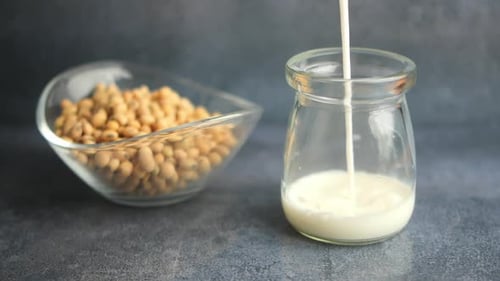 Pouring Soya Milk Into a Jar Next to a Bowl of Soya Beans