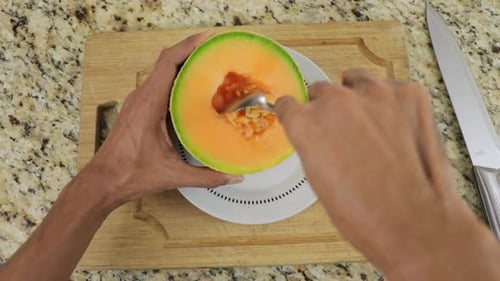 Hands of a man removing seeds of melon using a spoon. Closeup shot.