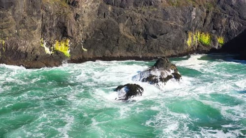 Scenic static aerial shot of ocean waves crashing along a rocky cliff side in Oregon, Pacific Northw