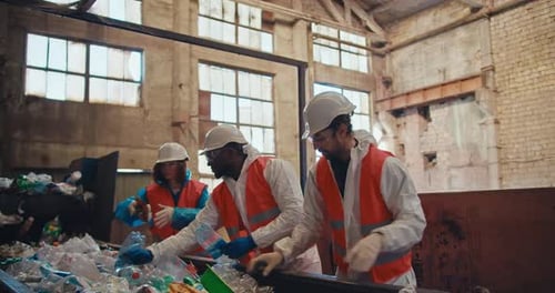 A Trio of Waste Recycling Plant Workers in Special Protective Uniforms and White Helmets Stand Near