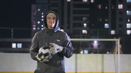 Athlete Smiling While Holding Soccer Ball on Urban Field at Night