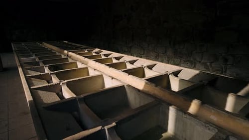 Chambre en pierre faiblement éclairée avec une longue structure en treillis de béton, peut-être d'anciennes cuves industrielles, en P...