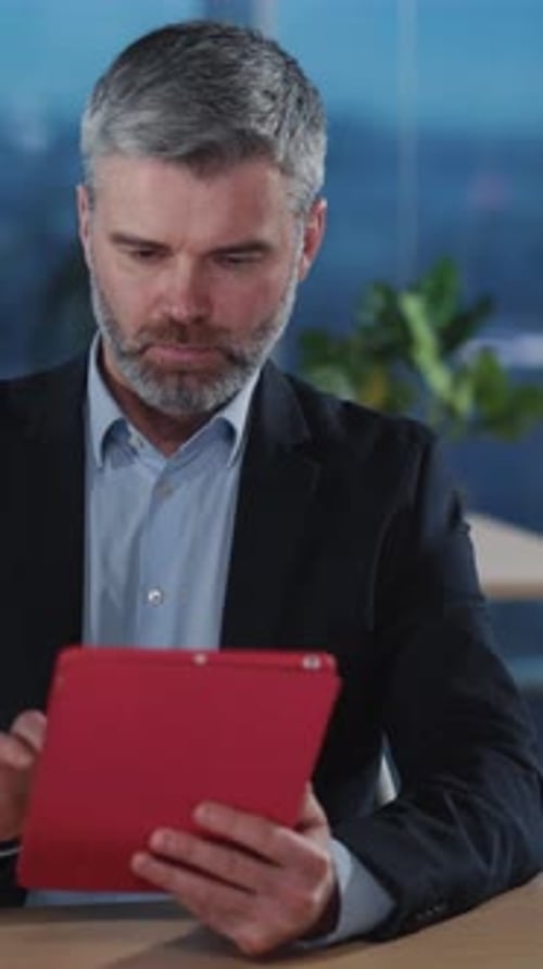 A Focused Businessman is Engaged Using a Tablet While Sitting in a Modern Office Environment