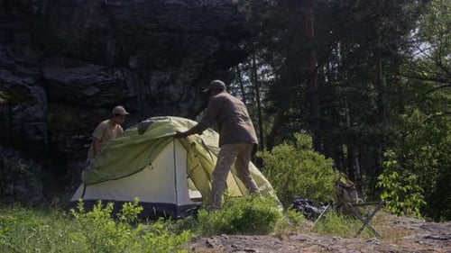 Mature Man and Teenage Boy Assembling Camping Tent in Forest