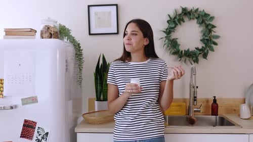 Woman Enjoys Yogurt Snack in Bright Kitchen
