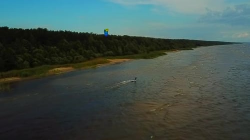 Wider view from above of a kite surfer riding the waves.