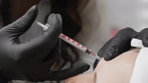 Ein Mediziner in schwarzen Handschuhen verabreicht vorsichtig eine Injektion in einer Nahaufnahme