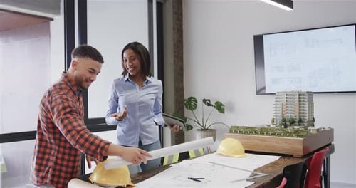 Happy diverse male and female architects with tablet discussing blueprints in office, slow motion