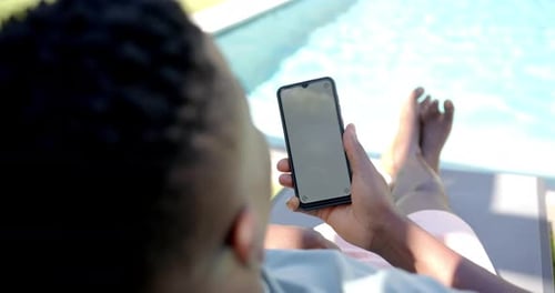 Relaxing by pool, person using smartphone while lounging on chair, copy space