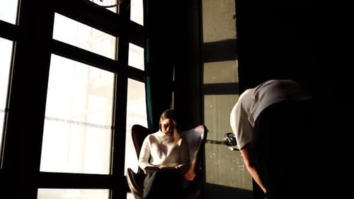 Model and videographer in natural light studio with vintage chandelier and chair