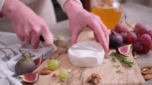 Femme tranchant du camembert ou du brie sur une planche à découper en bois dans une cuisine domestique