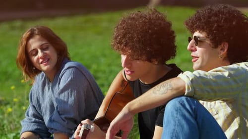 sing together - young friends sitting on the lawn at park sing together