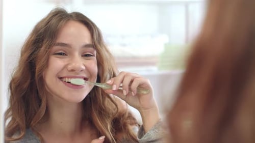 Smiling Woman Brushing Teeth in Bright Bathroom
