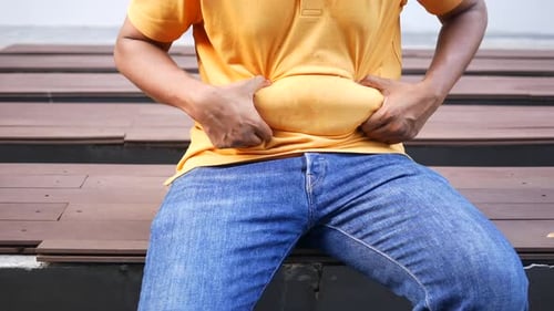 Man Holding Stomach Outdoors in Jeans and Shirt