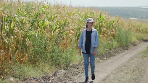 Caucasian Female Farmer Walking on a Dirt Road Among Cornfields During Daytime