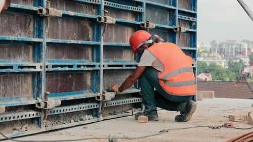 A Builder at the Construction of a Highrise Building Drives a Nail with a Big Hammer A Construction