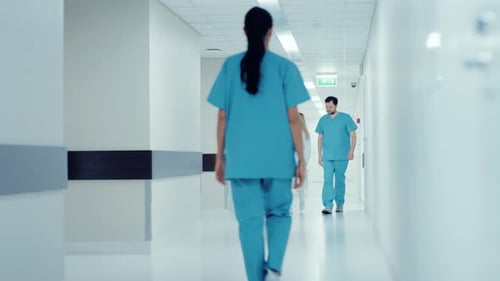 Team of Doctors, Surgeons and Nurses Walk Through Busy Hospital Hallway, They Talk about Patients,
