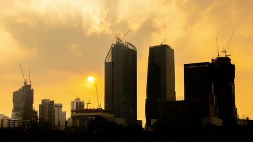 Sunset silhouette time lapse video of tower cranes working on site project in a city.