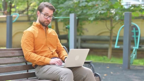 Man Works on Laptop in Urban Park on Bench
