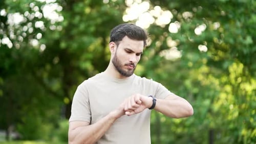 Sports man stands in urban city park and looking smart watch. Handsome smiling athlete using fitness