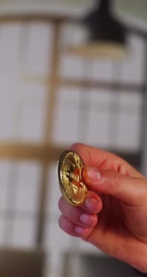 A close-up shot of a hand holding a shiny gold-colored Bitcoin coin, showcasing the cryptocurrency s