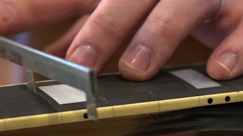 Un técnico de reparación de primeros planos utiliza una sierra de fresado para canalizar las ranuras de los trastes de la guitarra