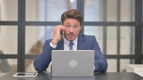 Man in Suit Talking on Phone at Desk