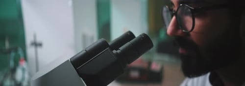 Close Up Face Man Scientist with Glasses Looking Under a Microscope in a Light Laboratory Medicine