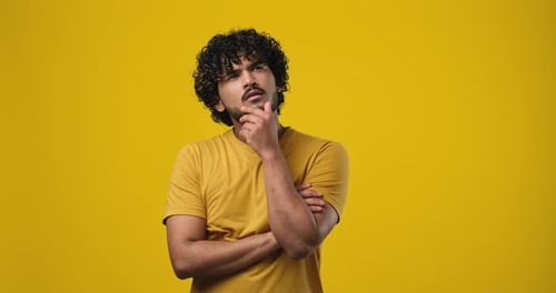 Young Indian Man Thinking with Hand Near Chin Standing Over Studio Background